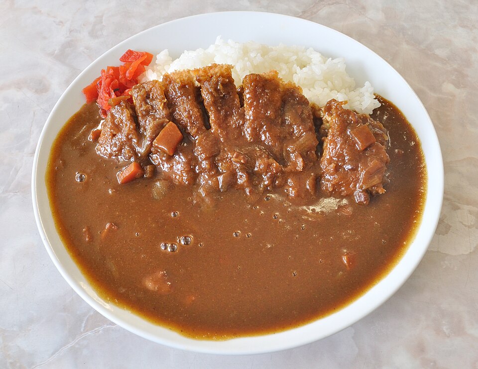 Photo of a katsu curry served at the Japanese equivalent of a diner. A katsu cutlet, brown curry sauce, white rice, and bright red fukujinzuke are the prominent elements.