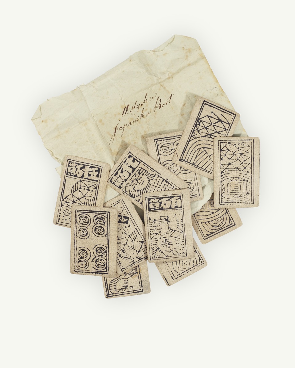Photo of eleven madiao cards in front of a torn page incorrectly identifying them as "Japanese playing cards". The cards are illustrated and printed in stark black on white.