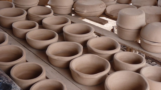 Photo of handmade pottery on an outdoor table. Over two dozen slightly different pots are arranged in rows.
