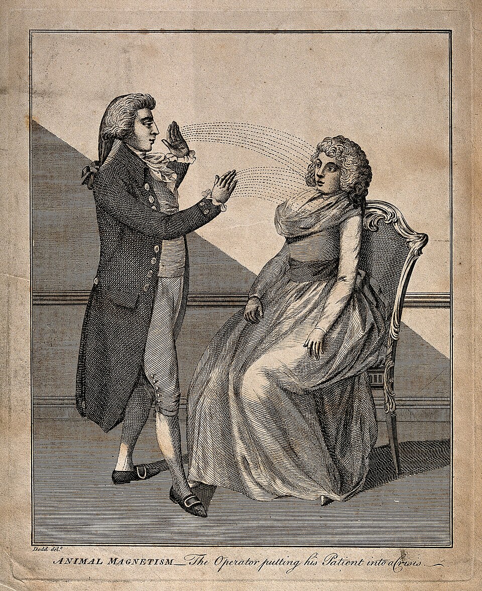 1802 engraving of a man mesmerizing a woman with animal magnetism. The man is wearing a powdered wig and a coat. He stands on the left and uses his arms to manipulate the life force. The woman is sitting in a fancy chair and wearing a long dress.